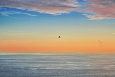 Small plane fly across the ocean at sunset